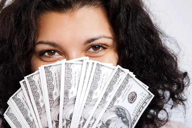 A woman cover parts of her face using a stack of cash as example of financially independent women.