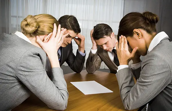 A group of 4 corporate workers cracking their head and looking on a blank white paper.