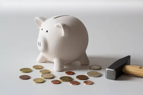 a hammer next to a white piggy bank with coins for emergency fund