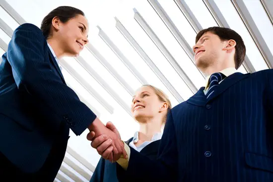 2 corporate sales person shaking hands while another looking on.