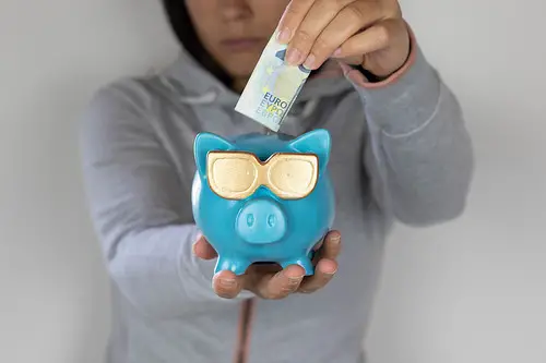 a woman putting paper money inside a blue piggy bank for retirement.