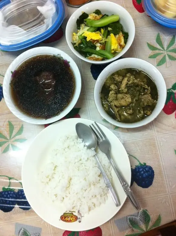 a confinement meal with white rice, herbal soup, spiced meat and kailan with egg.