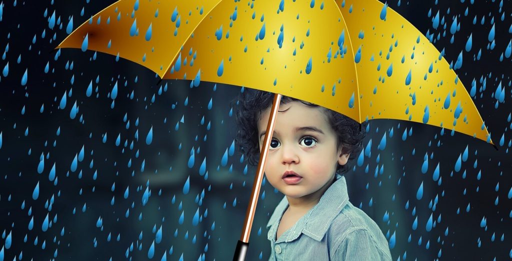 A little boy protected by umbrella from rain drops as an example of child medical insurance