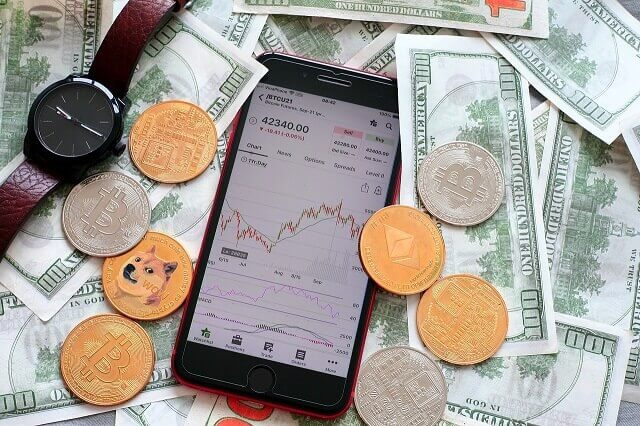 Digitalcoins, dollar bills, a phone with crypto chart and a watch representing the right time to buy cryptocurrency.
