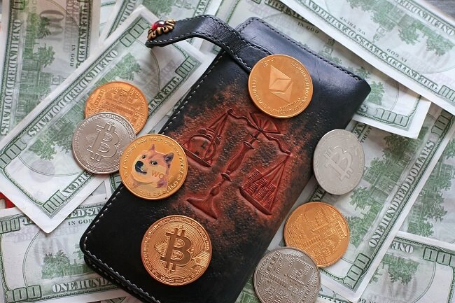 various crypto coins on top of a wallet and paper money representing buying first crypto.
