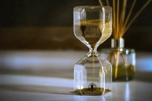 An hourglass with olive colored sand representing waiting period.